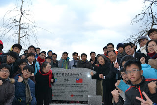 「台湾の皆さんありがとう」と刻まれた石碑の周りに集まった台湾からの修学旅行の一団がガッツポーズなどのポーズをしている記念写真