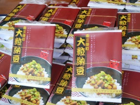 ごはんの上に大粒納豆が乗った写真と、「大粒納豆」と書かれた赤いパッケージに入った大粒納豆の商品が重ねて積まれている写真