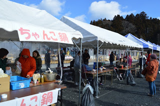 「ちゃんこ鍋」の看板を掲げた白いテントの中で数名の女性が作業をしている写真