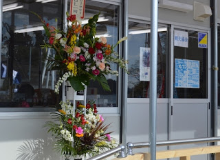 店舗の入り口前に飾られた2段のお祝いのフラワーアレンジメントの写真