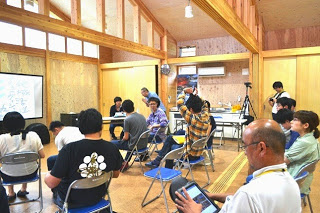 木の温もりがある室内で参加者たちが椅子に座り、セミナーが開始されるのを待っている様子の写真