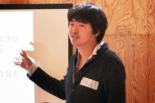 スクリーンの前に立った男性が、スライドを指さしながら説明をしている様子をアップで撮影した写真