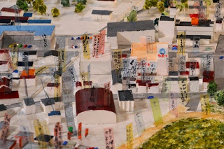 色とりどりの屋根の民家や建物の上に細かく書かれた文字入りのラベルが多数立てられている、町中の模型の詳細写真