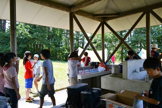 屋根付きの炊事場で子どもたちが食器の準備や水のくみ取りなどをしているキャンプの炊事の写真