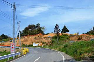 山の斜面で土木作業が進んでいる道路沿いの工事現場の写真
