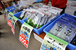 長机の上に青いかごが並び、それぞれポップが貼られた異なる種類の海藻製品が並べられている海藻販売の写真