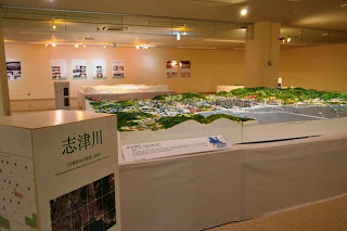 「志津川」と書かれたパネルの前に、町や港の立体模型が広がっている様子の写真