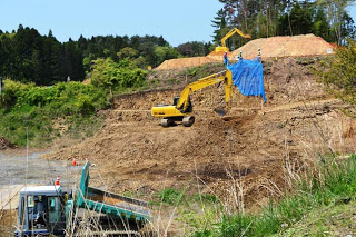 斜面に青いシートがかけられ、その近くで重機が土を掘削している様子の写真
