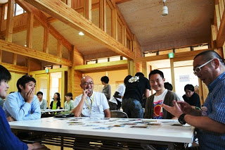 木の内装に囲まれた明るい室内で、複数人がテーブルを囲みながら意見を交換している様子の写真