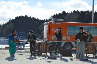 カラフルな衣装を着た男性と、三味線を持った袴姿の男性、法被を着て笛や太鼓を演奏している男性3人がステージを盛り上げている写真