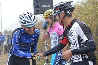 ヘルメットをかぶった青い服の自転車選手と竹谷賢二さんが、互いに笑顔で握手し、交流している写真