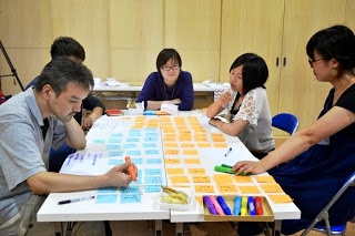 参加者たちが白いテーブルを囲み、カラフルな付箋に文字を書きながら真剣に話し合っている ワークショップの様子の写真