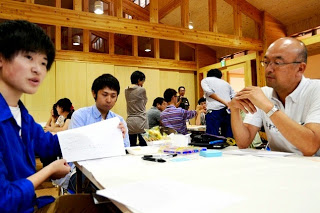 3人の男性の参加者のグループが、真剣な表情で資料を手に取りながら向き合って議論している様子の写真