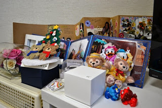 テレビが設置された台の上に、沢山の写真が貼られたアルバムや2体のダッフィーぬいぐるみ、青と赤色の小さなシーサーの置物が飾られている写真