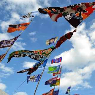 青空に白い雲が浮かぶ中、竹につるされた様々な模様や文字が描かれた色とりどりの大漁旗が風に揺れている様子の写真