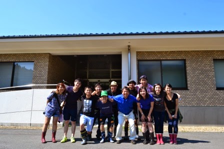 現場見学で伺った、ベージュ色の外壁の建物の前に長靴姿の参加者たちが並び、笑顔で記念撮影している集合写真