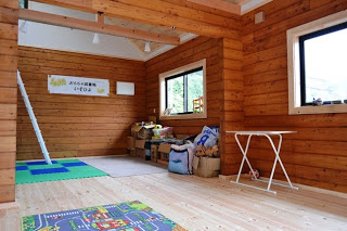 木の壁と床で囲まれ、ジョイントマットが敷かれた室内に折り畳み式のテーブルやおもちゃが整えられている室内の写真