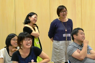 5人の男女が椅子に座ったり立ったりしながら笑っている、リラックスした雰囲気の中で楽しんでいる様子の写真