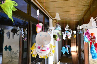 廊下の天井から、子どもたちが作ったカラフルな手作りの飾りが沢山吊るされていて、縁側を彩っている写真