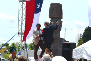 白サンゴの眼と黒曜石の瞳がはめ込まれたモアイ像の前に立つ二人の男性が握手を交わし、モアイ像の目元に手を置いて写っている開眼式の様子の写真