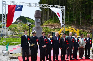 モアイ像の前にチリと日本の両国関係者の方々が横一列に並び、背後にチリ国旗と日本国旗が掲げられた中で記念撮影をしている写真