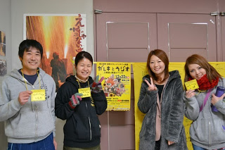 映画祭のポスターの前で、黄色いチケットを手に笑顔でピースサインをしている若者4人の写真