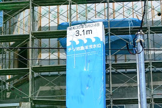 建設現場の足場の手前に高さ3.1メートルの洪水浸水位を示しており、その上に昭和35年5月24日と書かれている青い標識の写真