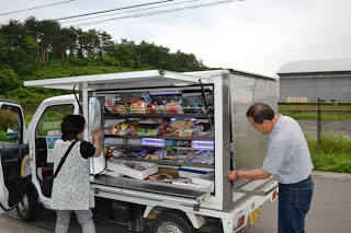 軽トラックの側面を大きく開けると、中には魚や惣菜などの商品がぎっしり並べられており、及川夫婦が移動販売の準備をしている様子の写真