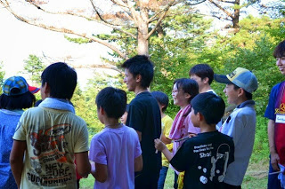 様々な色の服を着た子どもたちが、楽しそうに外で何かを見たり話したりしている集団活動中の写真