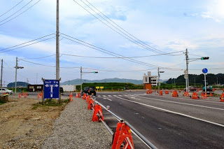 舗装道路に沿ってオレンジ色のバリケードが並ぶ中、信号機のある交差点を車が通行している工事中の交差点の写真