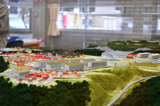 赤い屋根の住宅群や団地、施設などの大きな建物、道路、緑地などが含まれた町の詳細な縮尺模型が写っている写真