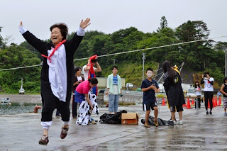 ペンギンの仮装した女性が笑顔でジャンプしている様子と、奥に別の参加者たちがコスチュームを着替えている様子が写っている写真