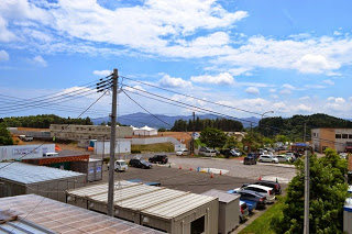 晴れた空の下、工事用のプレハブや資材置き場、駐車場などが見える建設予定地全体を高所から撮影した写真