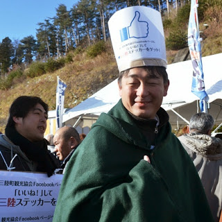 男性がフェイスブックの「いいね！」マークの帽子をかぶり笑顔で振り向いている、交流イベントを盛り上げるPR活動の様子を写した写真