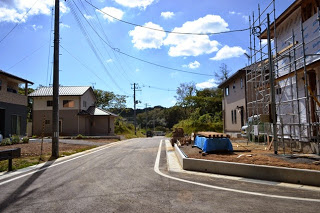 住宅街の新しい道路に沿って新築住宅が建ち並び、右手には足場が組まれた家の建設現場が見える、開発が進む住宅地の写真