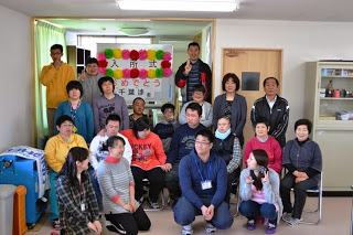入所式と書かれたホワイトボードの前で利用者やスタッフの方々が並んでいる記念写真