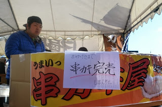 「おかげさまで、串カツ完売しました」と書かれた紙が貼られた屋台で、販売員が作業をしている人気商品の売り切れ後の様子を写した写真