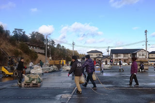 会場の片付け作業が進む中で、人々が荷物を運びながら歩き、フォークリフトも見える終了後の片づけの様子の写真