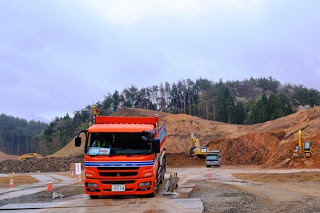 赤い大型ダンプカーが造成地の中を走行し、背景には重機や工事中の土の斜面が広がっている、造成地で働くダンプカーの写真