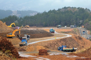 複数のショベルカーやダンプカーが稼働している造成地で、斜面や整備された道が広がる、宅地造成の工事現場を写した写真
