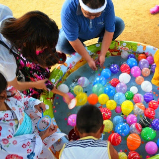 小さな子どもたちや浴衣姿の人々がビニールプールでヨーヨーすくいを楽しんでいる様子の写真