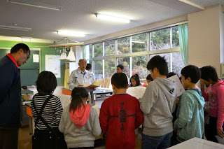 養蚕指導員 阿部一郎先生の周りに子どもたちが集まり、説明を聞いている様子を写した写真