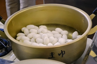 「まゆ」と書かれた鍋の中で、白い繭がたっぷりとお湯に浸かってゆでられている様子を写した写真