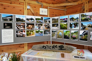 旅館や庭園の写真がパネルに多数並べられ、手前のテーブルの上には「かくれ里」と書かれた木製の看板が置かれている写真