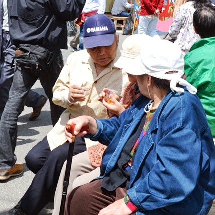 高齢の男女が杖を持って座りながら、手に持ったカップに入ったしらうおを楽しそうに味わっている様子の写真