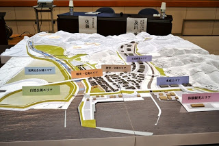 6つのエリアが付けられ、色分けされたゾーンで構成された、都市計画や開発プロジェクトを示す詳細な3D地形モデルの写真