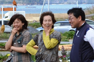 背景に海が見える場所で笑顔の女性二人と男性一人が楽しそうに会話している写真