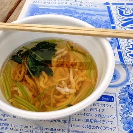 白い器に入った、小さな魚と青菜が浮かぶ透明なだしの汁物が、割り箸と一緒に紙のパンフレットの上に置かれている写真