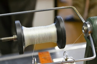 絹糸を巻き取る黒いボビンに細く透明な絹の糸が巻き付けられているアップの写真