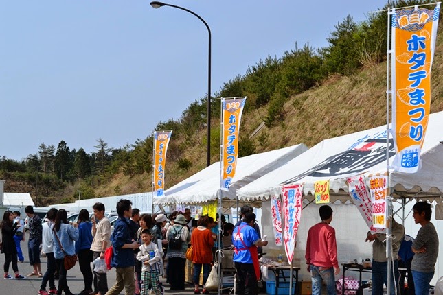 「ホタテまつり」と書かれたのぼり旗が立っている敷地内に設置された複数のテントが並び、沢山の人々が集まっている祭りの様子の写真